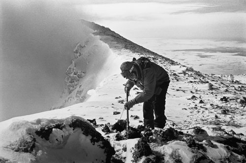 <p>Volcanologist Michael O&rsquo;Keefe examines the contents of a lava "bomb" at the 12,400 foot summit of Mt. Erebus.</p><p>"In 1984 the seismometers on the mountain were going wild. People on the other side of the Sound could see the bombs flying through the air in the night. Within thirty minutes after arriving on The Ice I was standing by the upper hut on Erebus. I walked just a few feet from the helicopter and there sitting on the ground was a lava bomb six feet across, smoldering. I jumped in the helo and said, &rsquo;Let&rsquo;s get the hell out of here!&rsquo;"<br/>—Dr. Philip Kyle</p>